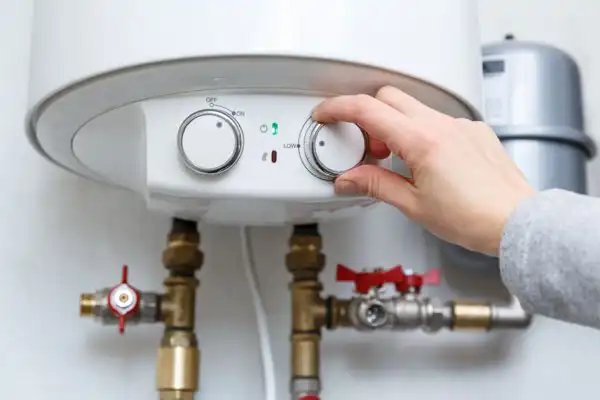 A hand expertly adjusts the temperature dial on a water heater, highlighting the meticulous attention required in boiler installation, with visible pipes and valves below.