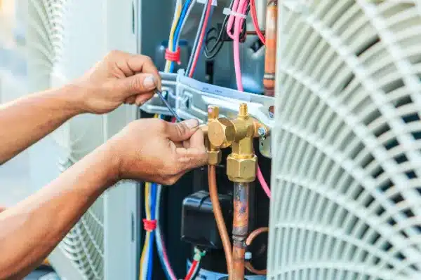 A person is diligently working on air conditioning maintenance, carefully using a wrench near various cables and pipes of the HVAC unit.