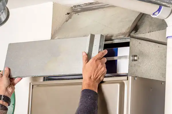 In a residential setting, an individual expertly performs furnace maintenance by carefully removing a metal panel from the furnace.